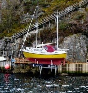 Red and yellow sailboat in Norway is lowered into the water using an IMM Quality elevator boat lift
